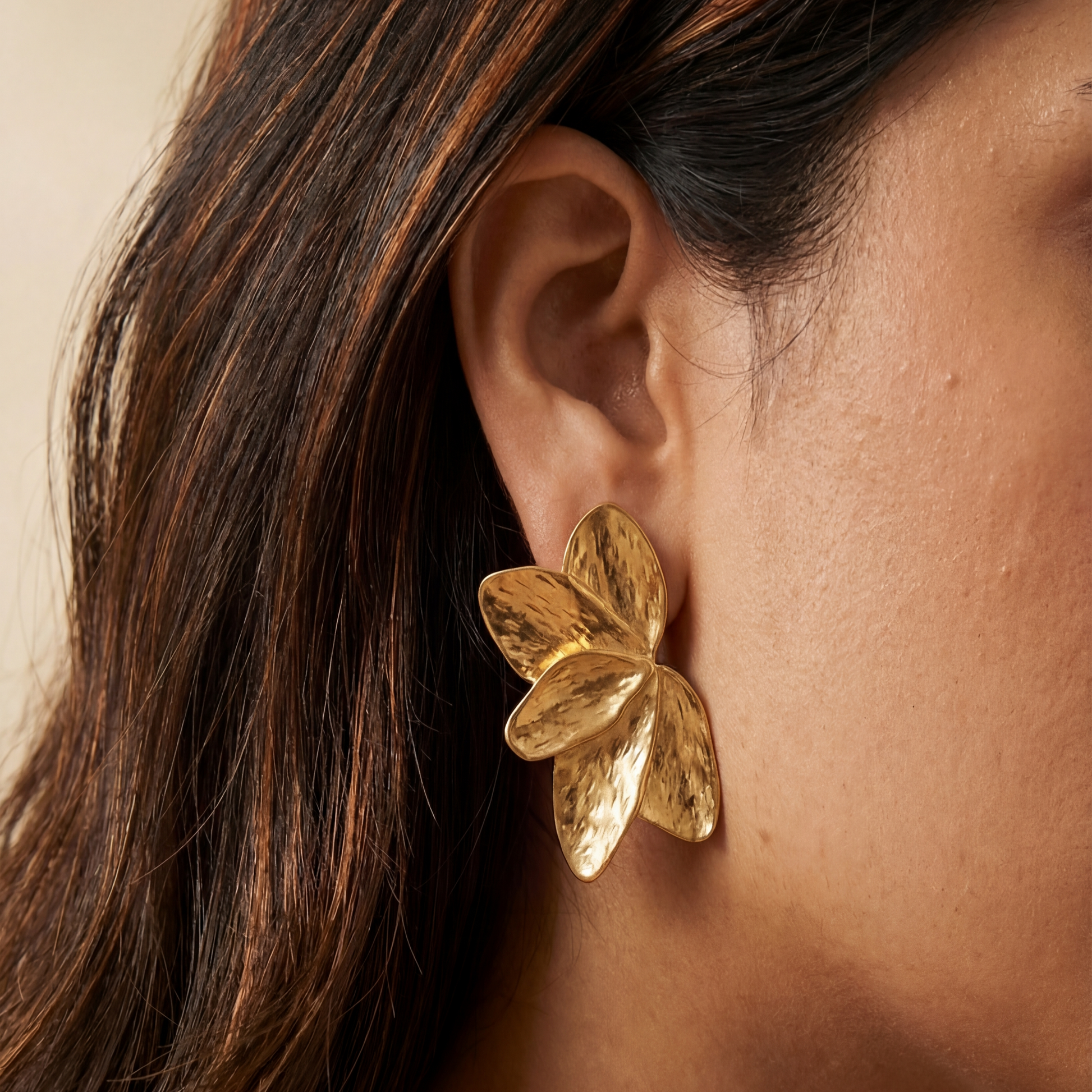 Gold leaf earring worn by a person with dark hair.