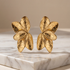 Gold flower-shaped earrings on a marble surface with a beige background