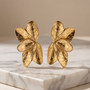 Gold flower-shaped earrings on a marble surface with a beige background