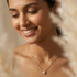Woman wearing a gold necklace with a clear pendant, surrounded by natural elements.