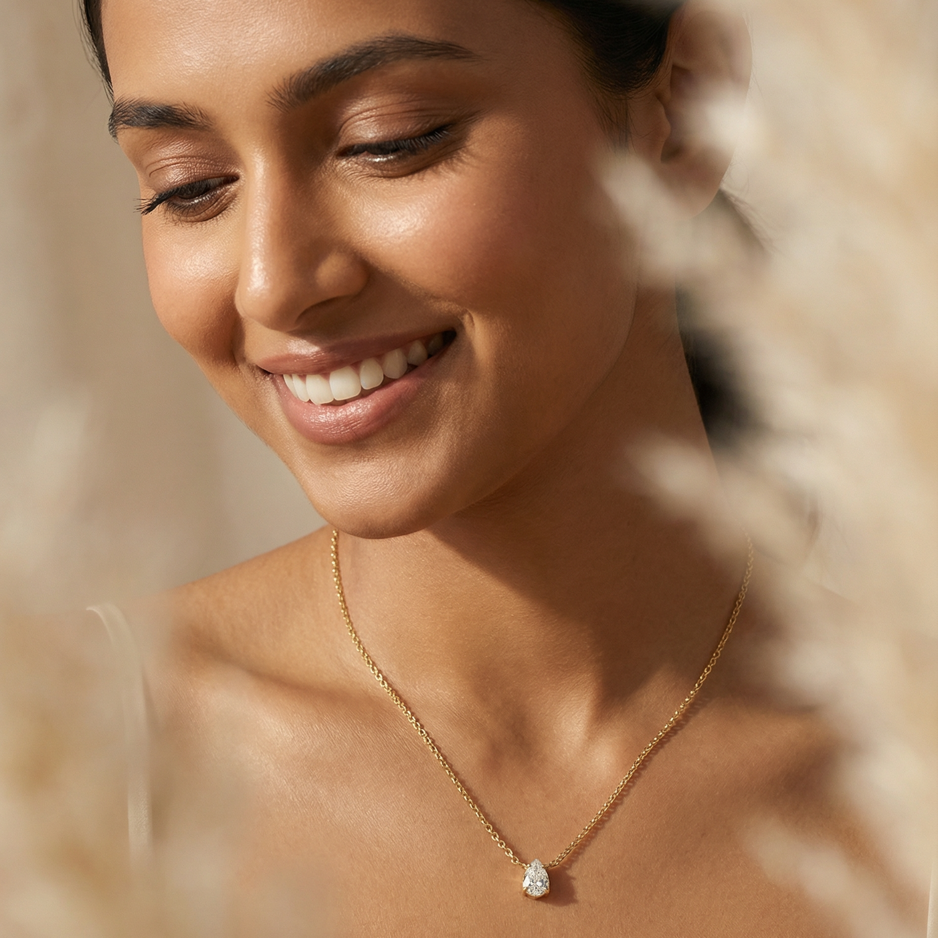 Woman wearing a gold necklace with a clear pendant, surrounded by natural elements.